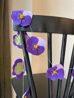 purple flowers are hanging from the back of a chair with black sticks and string attached to it