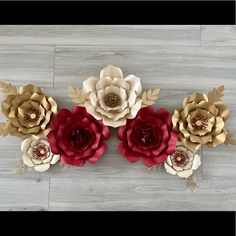 three paper flowers on a wood floor with one red and the other gold in it