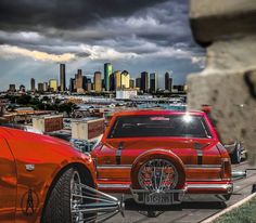 an orange car parked in front of a large cityscape with dark clouds above it