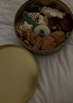 a christmas cookie tin filled with cookies on top of a white bed next to a round box