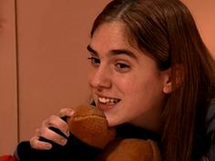 a young woman holding a teddy bear in her right hand and smiling at the camera