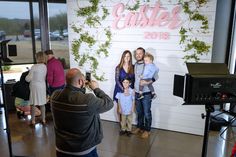 a group of people standing in front of a wall with greenery on it and one person holding a baby