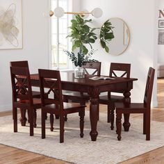 a dining room table and chairs in front of a potted plant on a rug