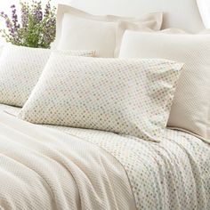 a bed covered in white sheets and pillows with polka dot print on them, next to a plant