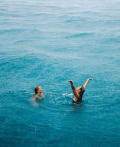 two people swimming in the ocean with one holding his arm out to catch something while the other looks up