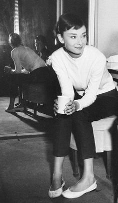 a woman sitting on top of a chair next to a table with a cup in her hand