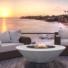 an outdoor fire pit sitting on top of a wooden deck next to the ocean at sunset