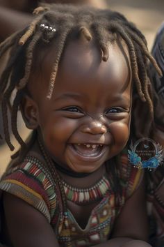 a smiling baby with dreadlocks on it's head and blue eyes smiles at the camera