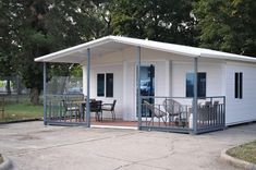 a small white house sitting in the middle of a park with tables and chairs around it