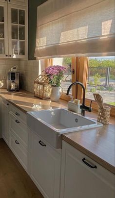 a kitchen with white cabinets and wooden counter tops, along with a window covered in roman shades