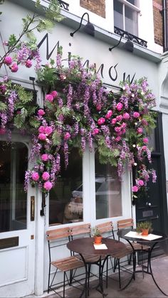 the outside of a restaurant with purple flowers growing on it's windows and tables