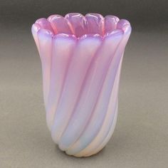 a pink and white glass vase sitting on top of a table next to a gray wall