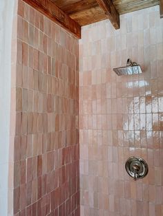 a bathroom with a shower head and pink tiles on the walls, along with a wooden ceiling