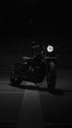 a black and white photo of a motorcycle parked in a parking lot with the lights on