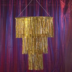 a chandelier hanging from the ceiling in front of a purple curtain with gold fringes