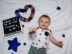 a baby is laying on a blanket next to some decorations and a sign that says, lookin'fly on my first fourth of july