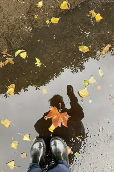 a person standing in front of a puddle with leaves on the ground next to it