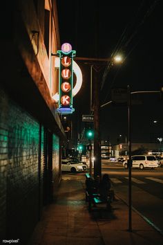 a neon sign on the side of a building next to a bench and street lights