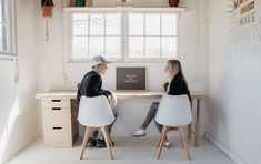 two people sitting at a desk in front of a window