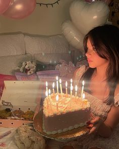 a woman sitting in front of a birthday cake with lit candles on it, surrounded by balloons