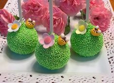 there are four cake pops decorated with flowers and bees on the top one is green