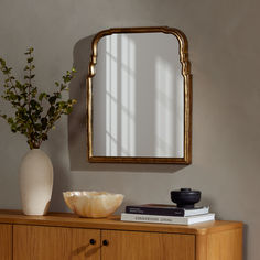 a wooden cabinet with a mirror and vase on it next to a wall mounted plant