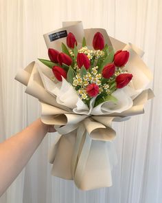 a bouquet of red tulips and daisies wrapped in white paper with ribbon