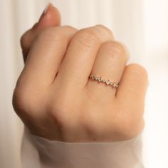 a woman's hand with a diamond ring on top of her finger, in front of a white curtain