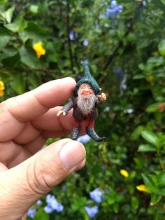 a small gnome figurine sitting on top of a persons hand in front of some flowers