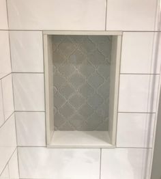 a white tiled bathroom with a square window in the wall and tile on the floor