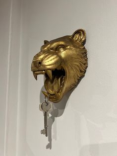 a gold lion head mounted to the side of a white wall with a key in it's mouth