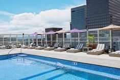 an outdoor swimming pool with lounge chairs and umbrellas next to the cityscape