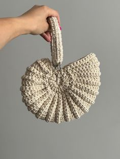 a hand holding a white knitted object in front of a gray background with the top part of it being held up