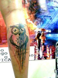 an owl tattoo is on the leg of a person in front of a painting and umbrella