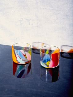 two glass cups sitting on top of a table next to each other with different colors