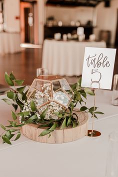 the table numbers are displayed on wooden slices with greenery and flowers in vases