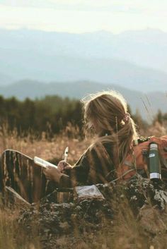 a woman sitting in the grass writing on her cell phone with a bible verse below