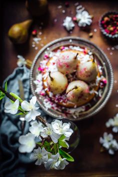 some food is sitting in a bowl on a table with flowers and pears around it