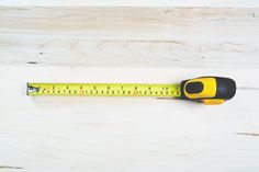 a yellow and black measuring tape on top of a white wooden table with a pair of scissors