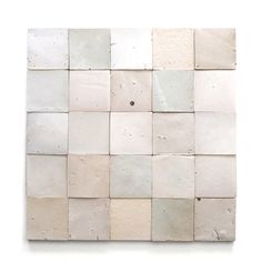 a white square tile wall hanging on the side of a building with several different colors and shapes