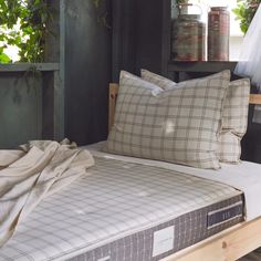 an unmade bed with two pillows and a sheet on the bottom, in front of some potted plants