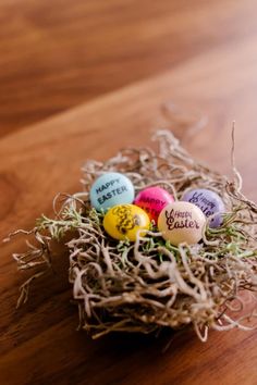 four eggs in a nest with the words happy easter written on them sitting on a wooden surface