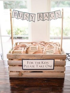 a wooden crate filled with lots of bags on top of a hard wood floor next to a sign that says busy bags for the kids please take one