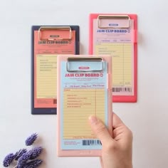 a hand holding a clipboard next to two binders with barcodes on them