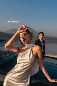 a woman in a white dress standing next to a car