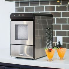 a silver microwave oven sitting on top of a counter next to two glasses filled with orange juice