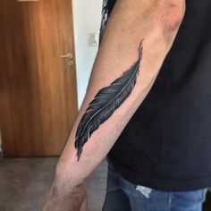 a man's arm with a black feather tattoo on the left side of his arm