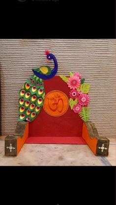 an orange and green peacock sitting on top of a red stand with flowers in it