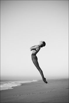 a woman jumping into the air on top of a beach