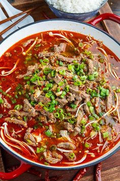 a bowl of beef and vegetable soup with rice on the side, ready to be eaten